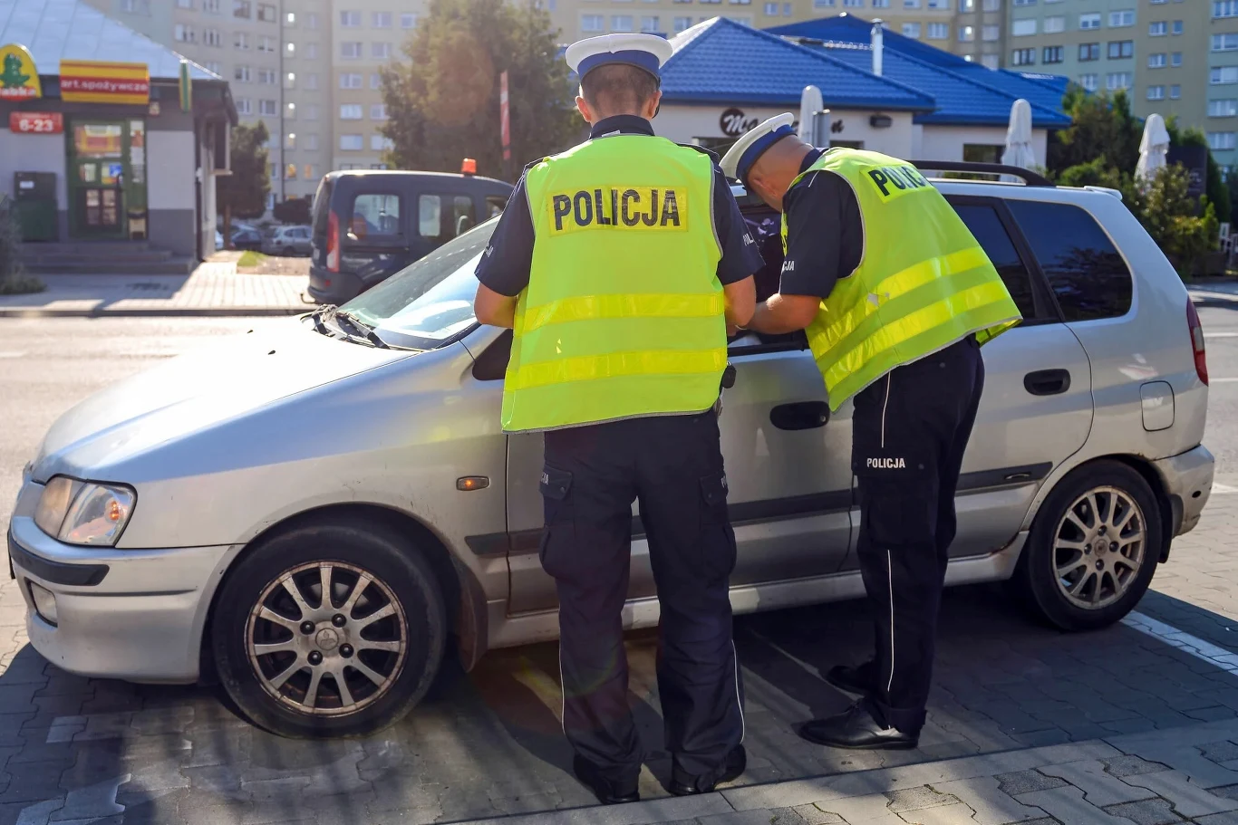 Za przewożenie niektórych rzeczy w samochodzie można dostać mandat Dwóch funkcjonariuszy policji w odblaskowych kamizelkach przeprowadza kontrolę drogowego pojazdu przy miejskiej ulicy, spisując notatki przy aucie osobowym.