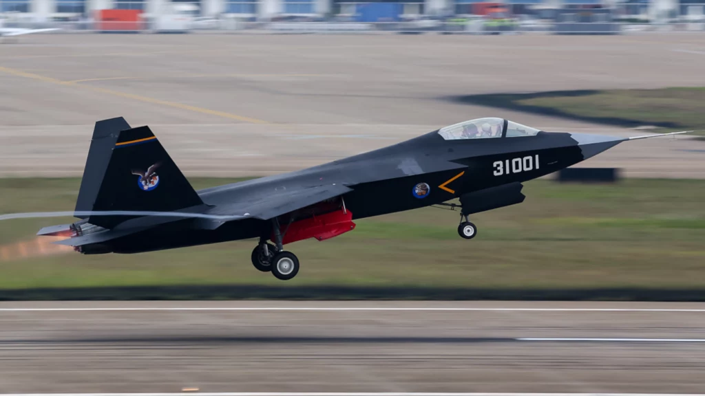 Podejrzewa się, że J-35 wywodzi się z projektu samolotu J-31. Na zdjęciu protorypowy J-31 na Zhuhai Air Show w 2014 roku Nowoczesny myśliwiec wojskowy startujący z pasa lotniska, samolot w ciemnym malowaniu z widocznym numerem taktycznym 31001, czerwone elementy pod skrzydłami oraz logo na stateczniku pionowym.