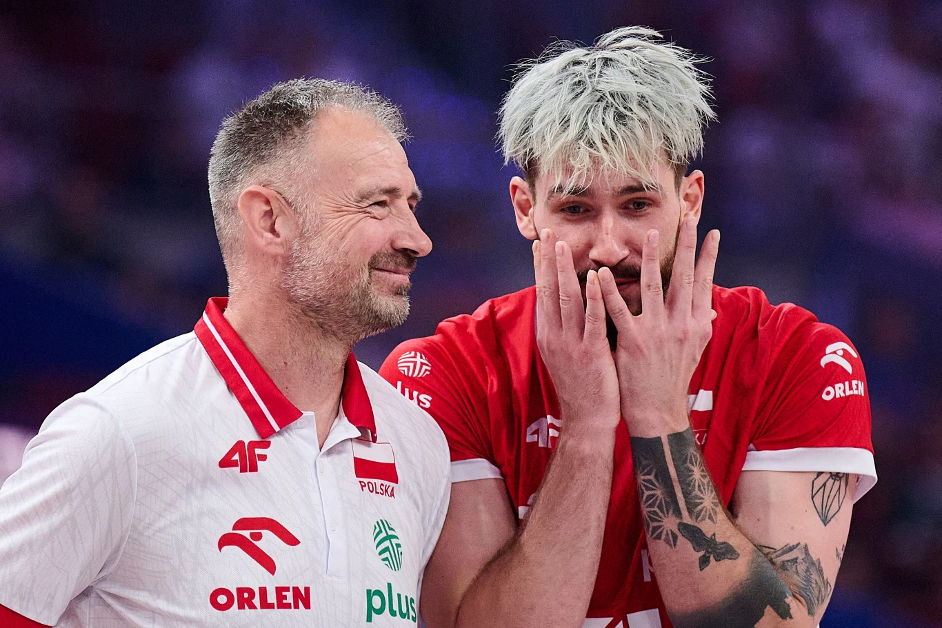 Nikola Grbić tonuje nastroje po meczu Polska - Francja Dwóch siatkarzy w czerwonych i białych koszulkach z logotypami sponsorów, jeden z nich uśmiecha się, drugi wydaje się być zaskoczony lub wzruszony, przykładając ręce do twarzy.