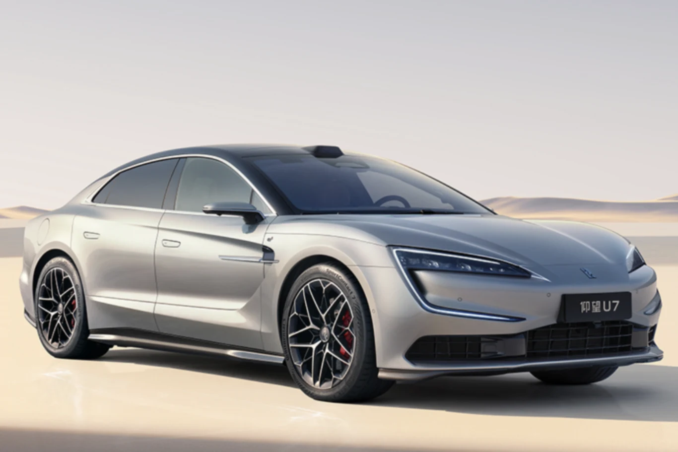 Nowoczesny, srebrny samochód elektryczny typu sedan o dynamicznej sylwetce, sportowe felgi i przyciemniane szyby, ustawiony na jasnym tle z delikatnymi wzgórzami na horyzoncie.