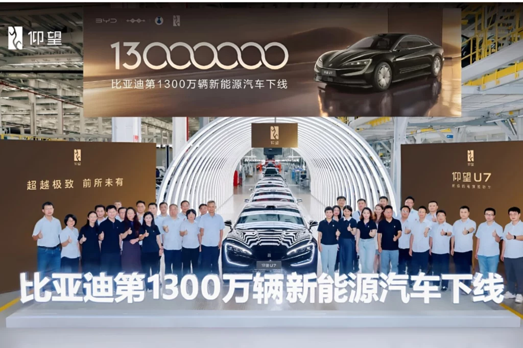 BYD świętuje - 13-milionowy pojazd opuścił fabrykę. Grupa ludzi stojąca przed nowoczesnym pojazdem elektrycznym na tle tunelu świetlnego w fabryce, bannery informujące o osiągnięciu 13 milionów wyprodukowanych samochodów oraz świętowanie ważnego momentu dla producenta motoryzacyjnego