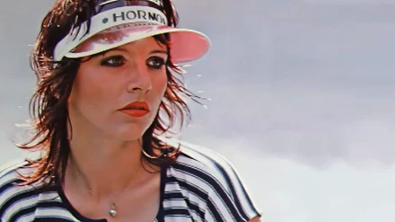 Jolanta Arnal Kobieta z makijażem i krótkimi, ciemnymi włosami, mająca na sobie bluzkę w biało-czarne paski oraz daszek przeciwsłoneczny z napisem, patrząca lekko w bok, na tle jasnego, jednolitego tła.