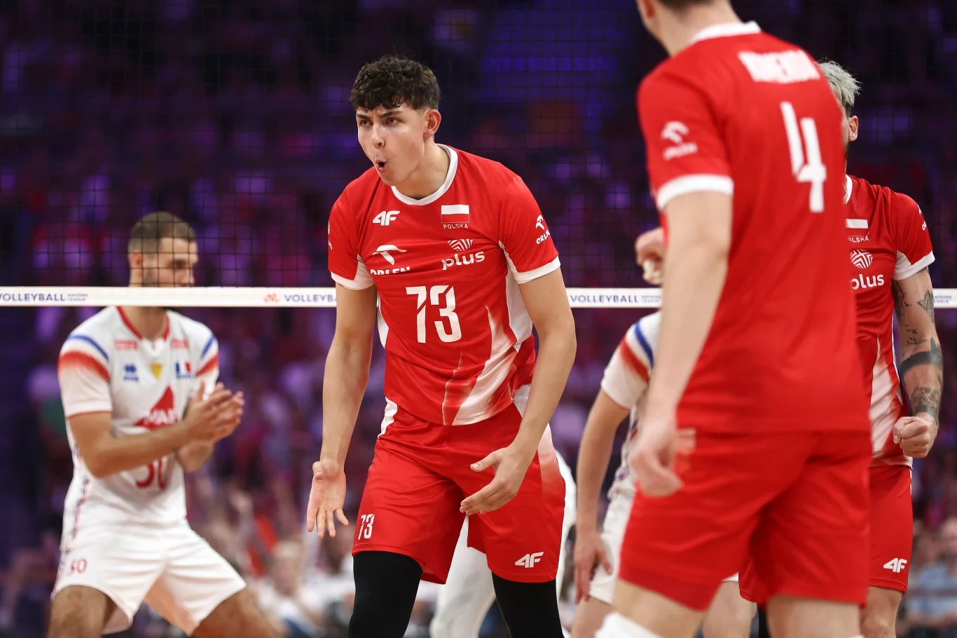 Jakub Nowak (z numerem 73) w meczu z reprezentacją Francji Zawodnik reprezentacji Polski w siatkówce w czerwonym stroju emocjonalnie reaguje podczas meczu, wokół niego inni gracze, sportowa hala w tle.