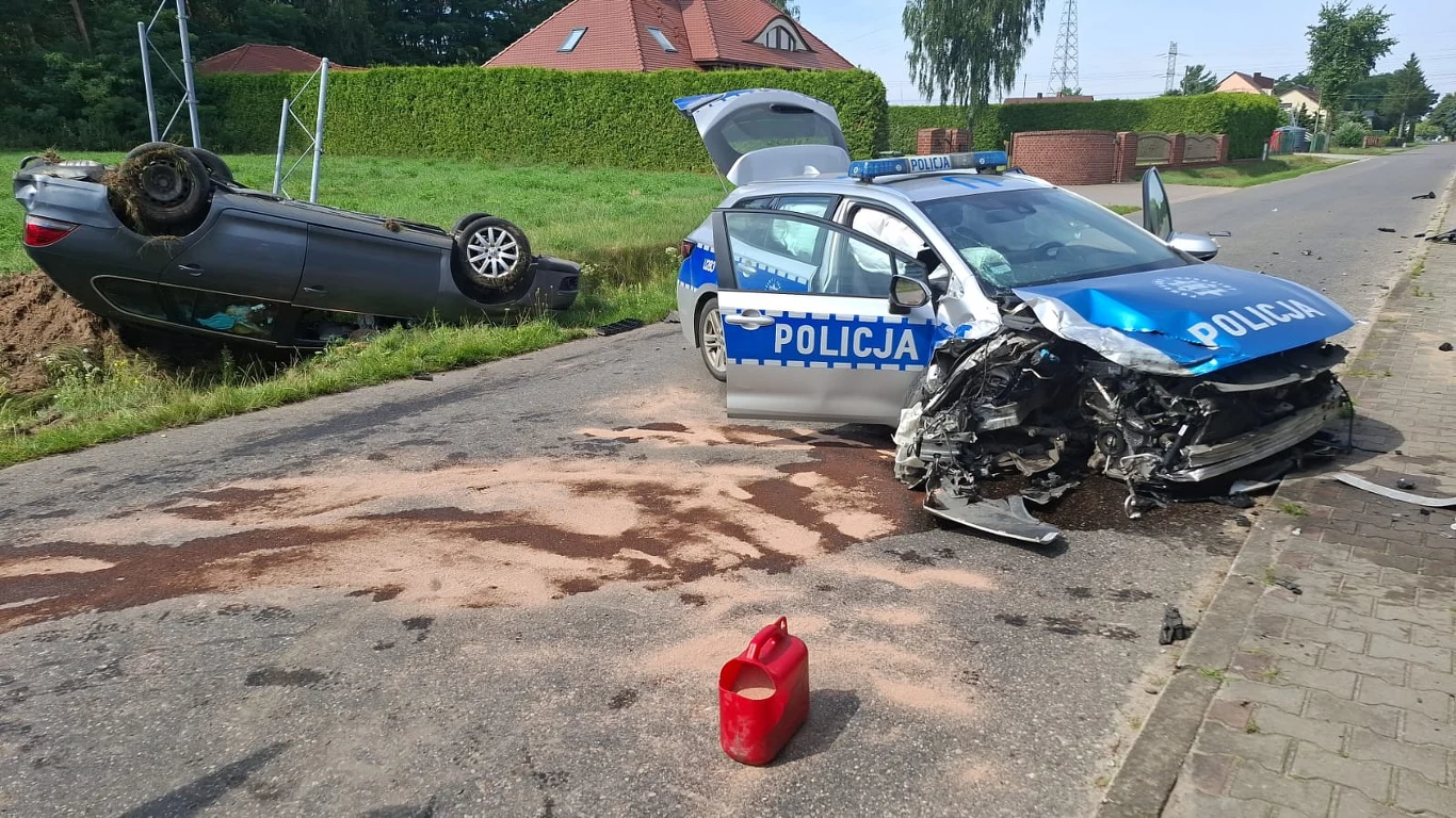 Wypadek w Teodorowie. Zdjęcie wykonane przez świadka zdarzenia Zderzenie rozbitego radiowozu policyjnego z innym samochodem, który leży przewrócony na dach w rowie przy drodze, przy samochodach widoczne uszkodzenia, na jezdni plamy po płynach oraz rozlana substancja, na pierwszym planie czerwona kanisterka.