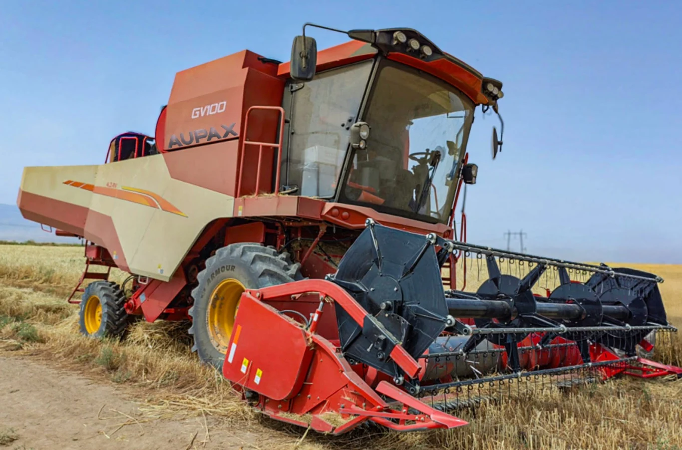 Maszyna, która właśnie została rozładowana w Tarnowie Podgórnym i trafia do testów pod marką Aupax, to model Weichai GV100. Kombajn zbożowy o czerwono-żółtej karoserii pracujący na polu podczas żniw, otoczony dojrzałym zbożem i niebem bez chmur w tle.