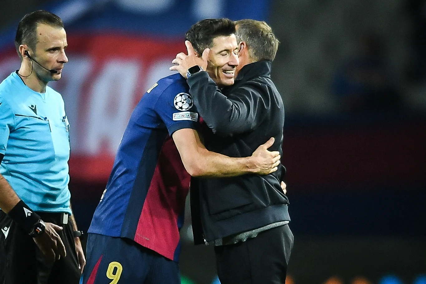 Robert Lewandowski i Hansi Flick Dwóch mężczyzn obejmujących się w przyjacielskim geście na boisku piłkarskim, jeden ubrany w strój sportowy z numerem 9, sędzia obserwuje sytuację z boku; w tle rozmazane barwy stadionu.