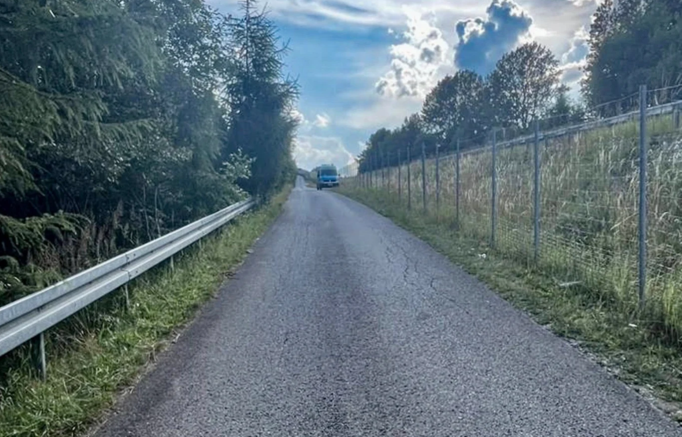 Tragedia przy trasie S1. Nie żyje 12-latek Wąska asfaltowa droga otoczona z jednej strony barierką ochronną, a z drugiej strony ogrodzeniem z siatki, prowadzi pod niewielkie wzniesienie, gdzie w oddali widoczny jest zaparkowany samochód; po bokach drzewa oraz trawy, nad horyzontem pojawiają się...