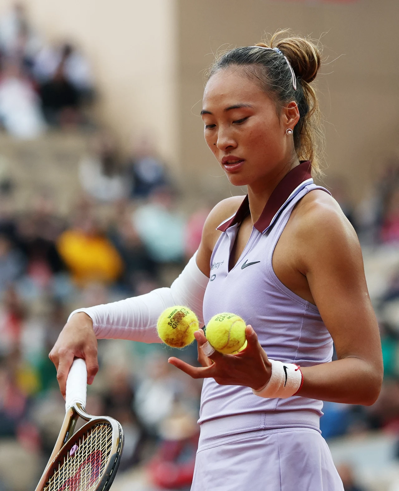 Qinwen Zheng Tenisistka w sportowym stroju trzymająca dwie piłki tenisowe oraz rakietę, skupiona na przygotowaniu do serwisu podczas meczu na korcie tenisowym.
