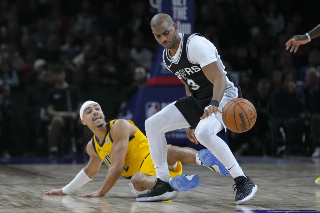Chris Paul Dwóch koszykarzy podczas dynamicznej akcji na parkiecie, jeden z zawodników w żółtym stroju siedzi na podłodze, a drugi w czarno-białym stroju kontroluje piłkę.