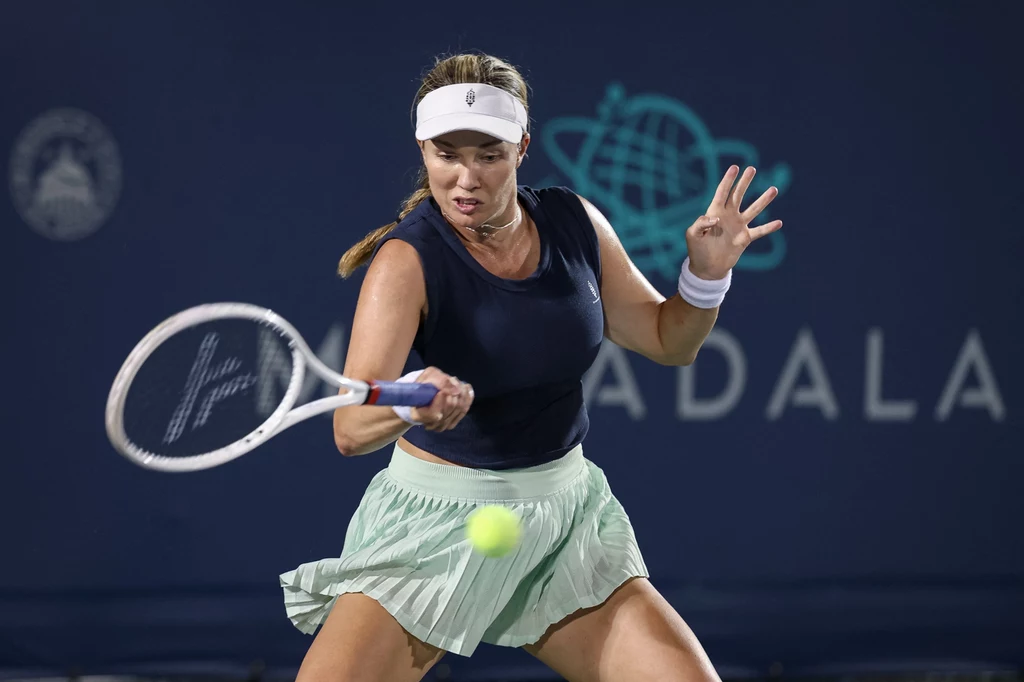 Danielle Collins Tenisistka skupiona podczas dynamicznego uderzenia piłki rakietą na tle ciemnego kortu, w sportowym stroju z opaską na głowie.
