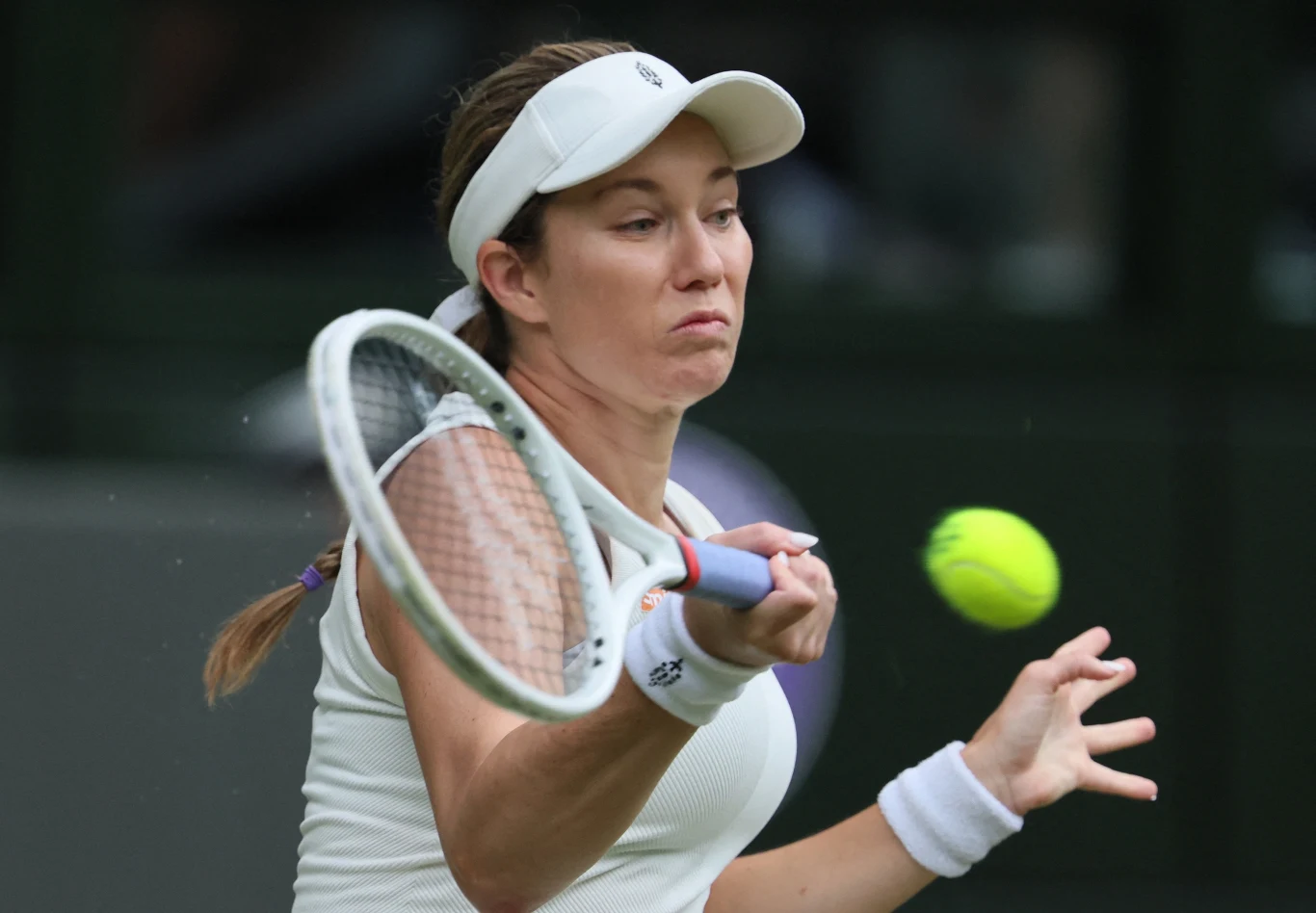 Tenisistka w białym stroju i czapce odbija piłkę rakietą podczas meczu tenisowego, skupiona na precyzji uderzenia.