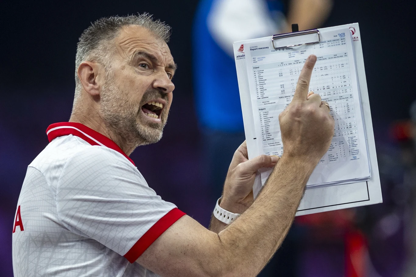 Nikola Grbić Mężczyzna w sportowej koszulce gestykuluje z zaangażowaniem, trzymając kartkę ze schematami i statystykami, wskazuje palcem na konkretne miejsce na dokumencie, wyrażając silne emocje.