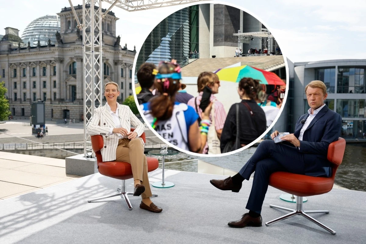 Wywiad na żywo wspóliderki AfD Alice Weidel zakłócony Dwóch prezenterów siedzących na czerwonych fotelach w otwartej przestrzeni z widokiem na budynek parlamentu, w tle widoczne nowoczesne budynki i duża okrągła wstawka pokazująca zbliżenie grupy ludzi idących pod kolorowym parasolem.
