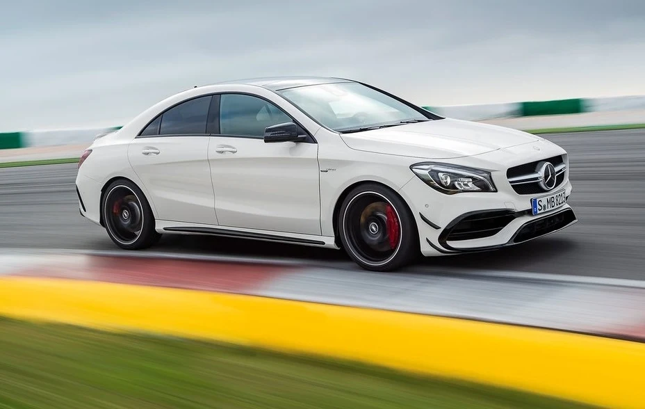 Biały samochód Mercedes-Benz klasy CLA podczas jazdy po torze wyścigowym, dynamiczny kadr z ostrym zakrętem, auto ma ciemne felgi i sportowy charakter.