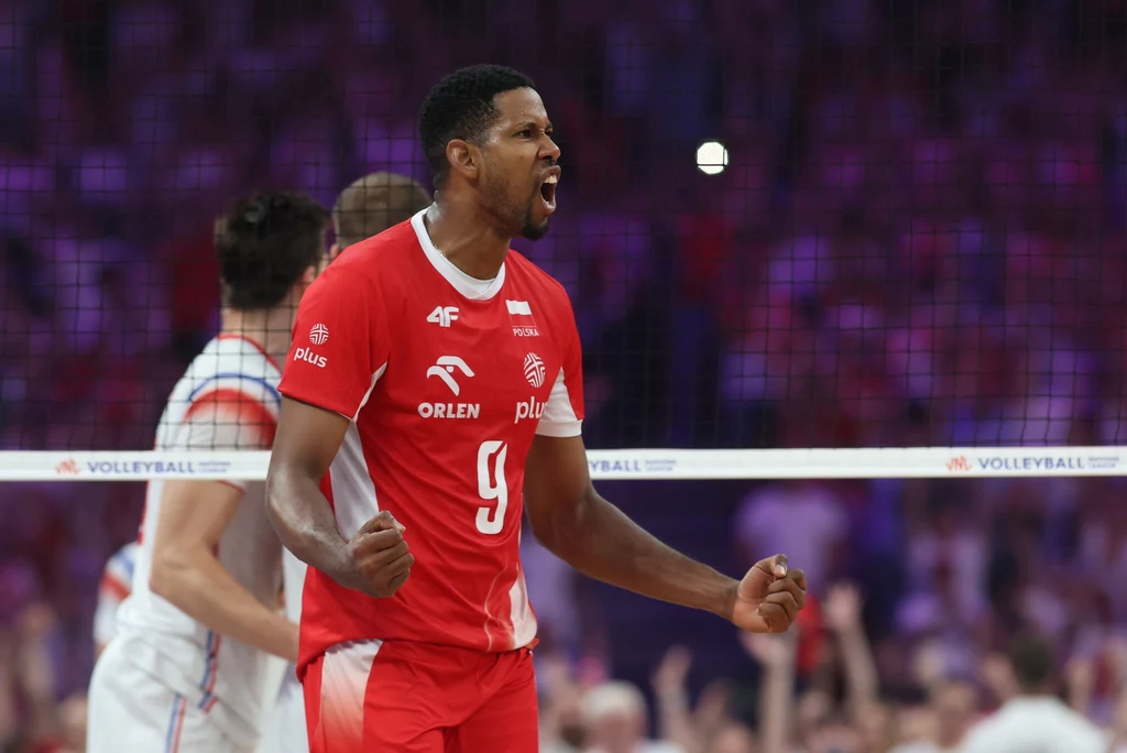 Wilfredo Leon Siatkarz drużyny narodowej w czerwonym stroju z numerem 9 wyraża radość i triumf na boisku, w tle siatka oraz zawodnik drużyny przeciwnej.