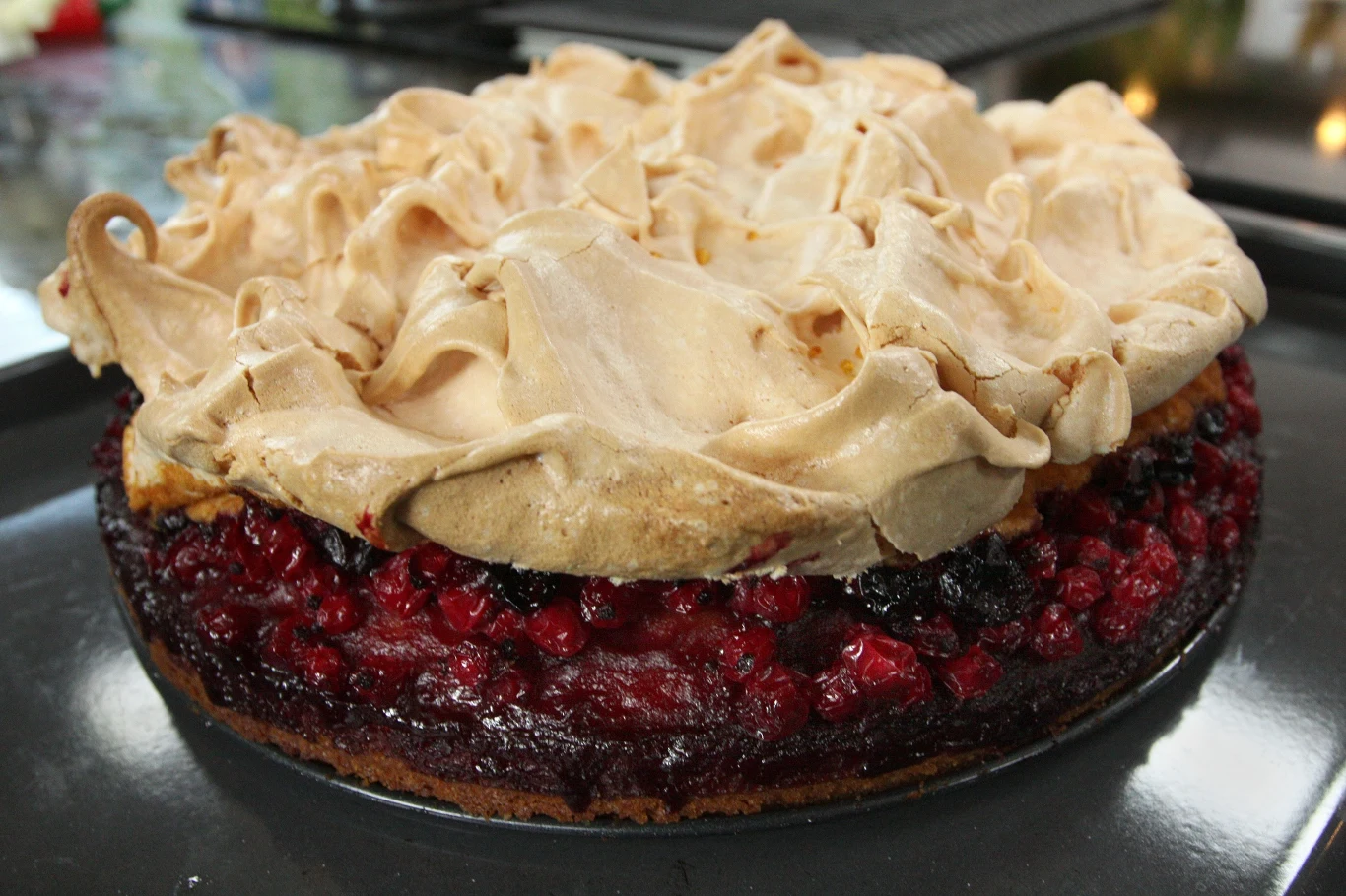 Ciasto z porzeczkami i bezą Ciasto z warstwą czerwonych owoców, takich jak porzeczki, przykryte chrupiącą bezą, podane na blasze do pieczenia.