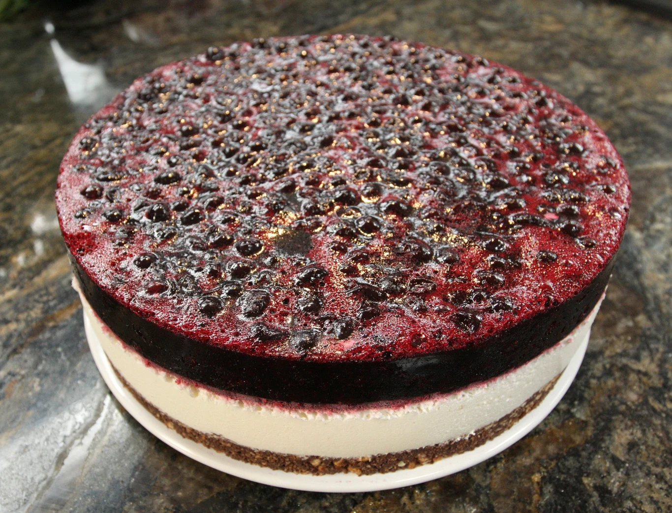 Torcik z musem porzeczkowym Okrągły jagodowy sernik na zimno z warstwą biszkoptowego spodu, grubą warstwą kremowego sera oraz gęstą, ciemnofioletową galaretką z jagodami na wierzchu.