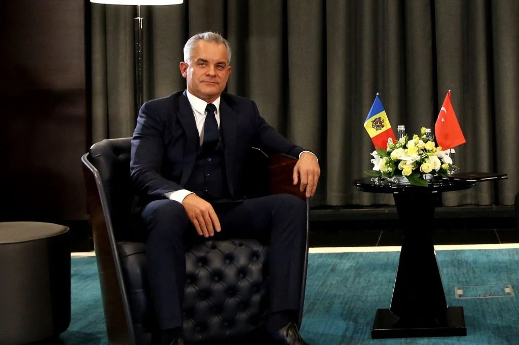 Vladimir Plahotniuc został aresztowany w Grecji Mężczyzna w eleganckim garniturze siedzi w czarnym, skórzanym fotelu, obok stoi stolik z bukietem kwiatów oraz małymi flagami Mołdawii i Turcji na ciemnym tle zasłon.