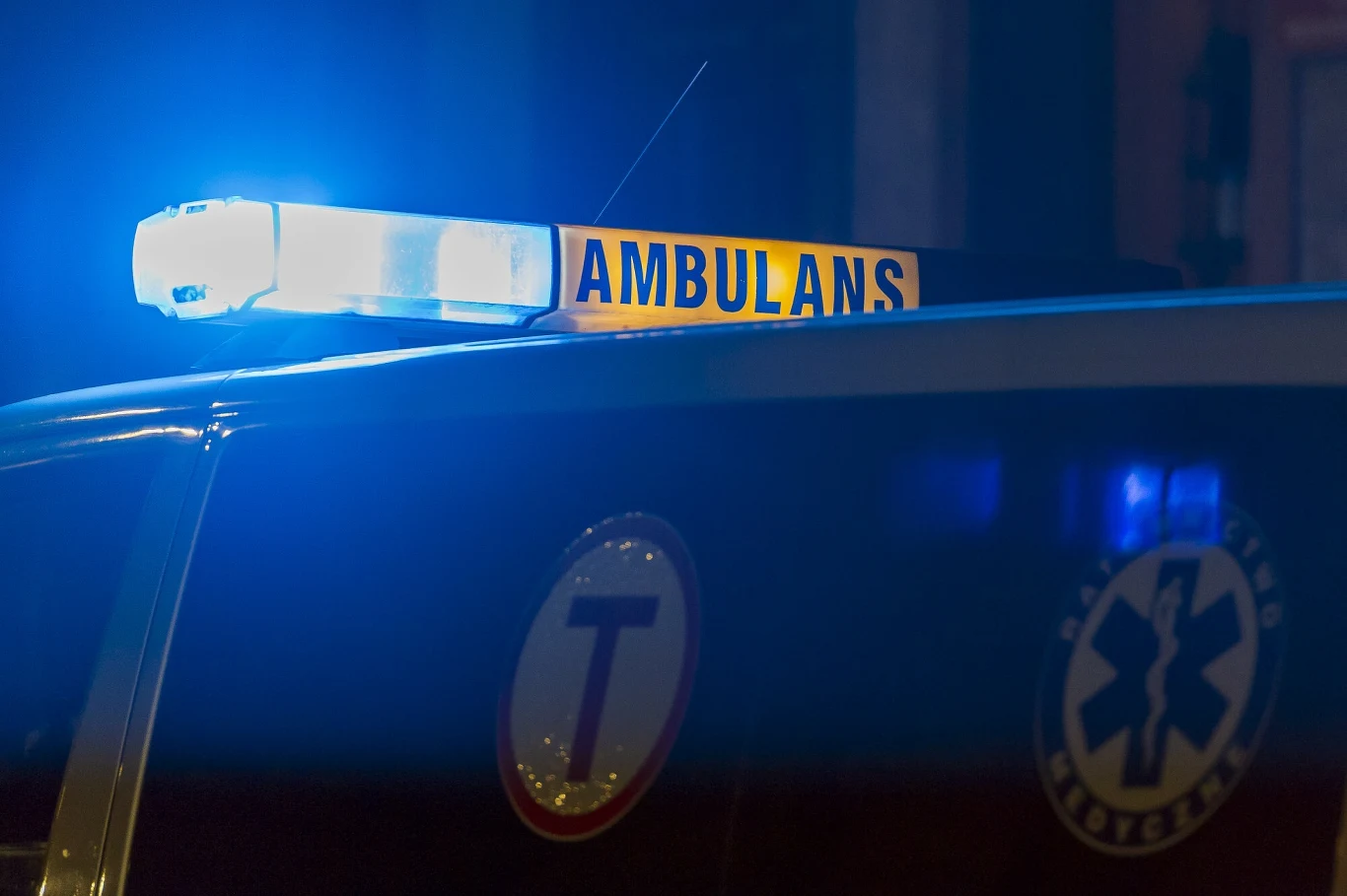 Niebieskie światło ostrzegawcze na dachu ambulansu, wyraźny napis 'AMBULANS' oraz symbol medyczny na karoserii pojazdu.