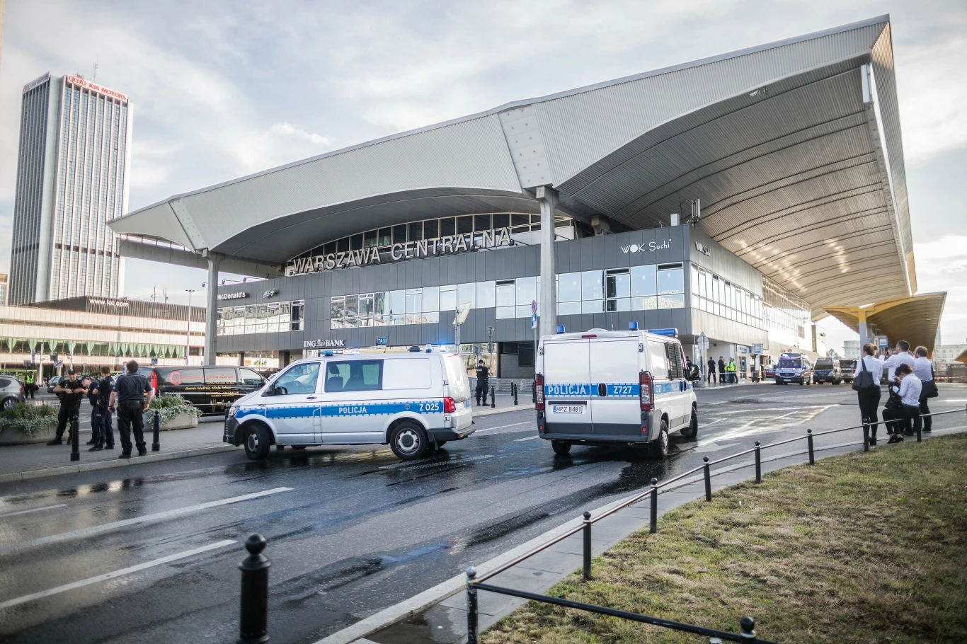 Pobicie przed dworcem Warszawa Centralna (Zdj. ilustracyjne) Warszawski Dworzec Centralny z dwoma zaparkowanymi radiowozami policyjnymi przed wejściem, obecnością kilku grup ludzi oraz charakterystyczną nowoczesną architekturą dworca na tle wysokiego budynku biurowego.