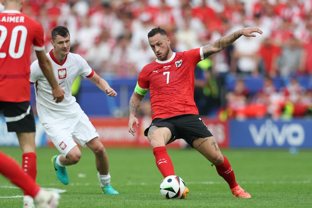 Marko Arnautovic dał się we znaki reprezentacji Polski Piłkarz w czerwonej koszulce reprezentacji Austrii kontroluje piłkę podczas meczu piłkarskiego, a obok niego biegnie zawodnik w białym stroju reprezentacji Polski, na trybunach widoczny tłum kibiców.