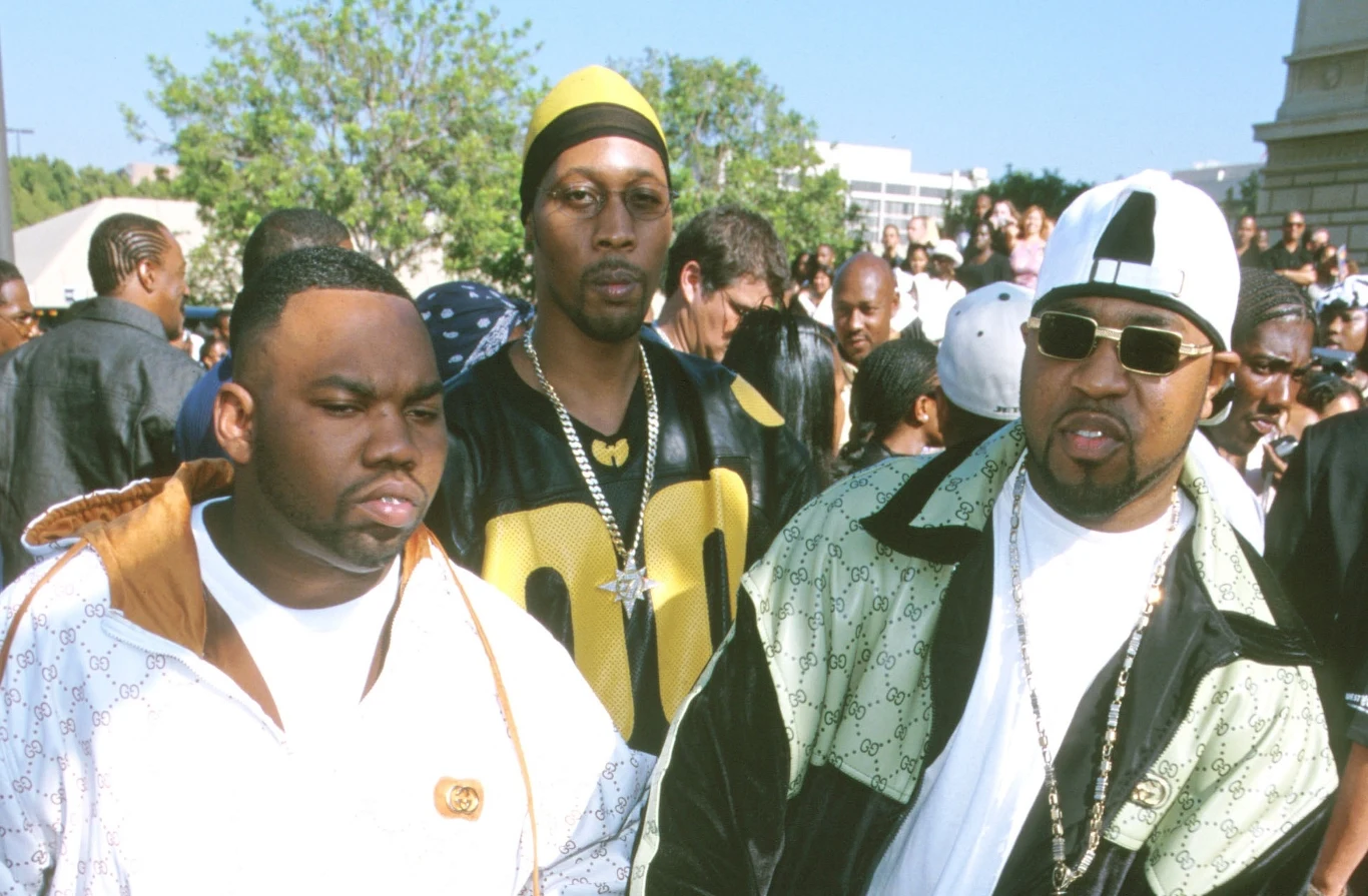 Kolekcjonerski album Wu-Tang Clanu ma nowego nabywcę Trzech mężczyzn ubranych w modne, sportowe ubrania stoi na zewnątrz w tłumie ludzi. Dwóch z nich nosi białe i czarne kurtki, jeden ma charakterystyczną czapkę i okulary przeciwsłoneczne. W tle widać innych uczestników wydarzenia oraz drzewa i budynki m...