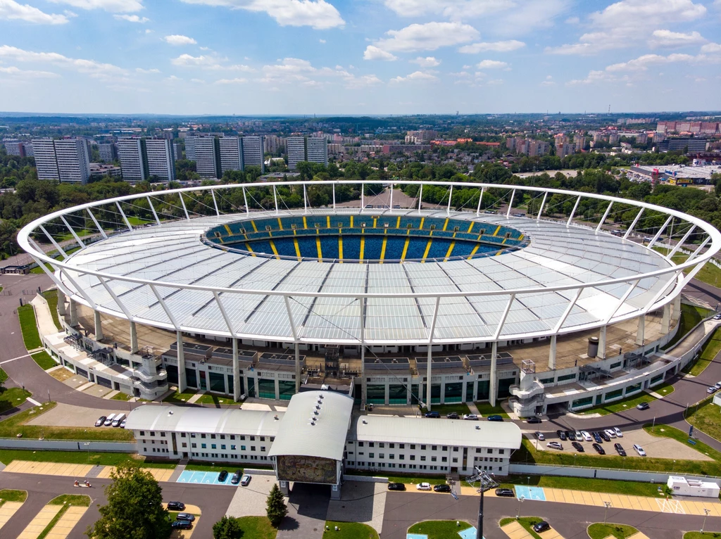 Stadion Śląski Nowoczesny stadion piłkarski otoczony miejską zabudową, widoczny z lotu ptaka, z wyróżniającą się białą konstrukcją dachu oraz wysokimi trybunami, wokół stadionu zaparkowane samochody, w tle panorama miasta.