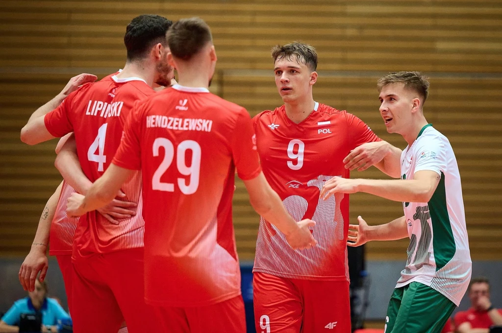 Polscy siatkarze na Uniwersjadzie Grupa zawodników podczas meczu siatkówki, trzech ubranych w czerwone stroje z napisem POL, jeden w białym stroju z zielonymi elementami, dynamiczna scena gry sportowej, gesty komunikacji i skupienia.