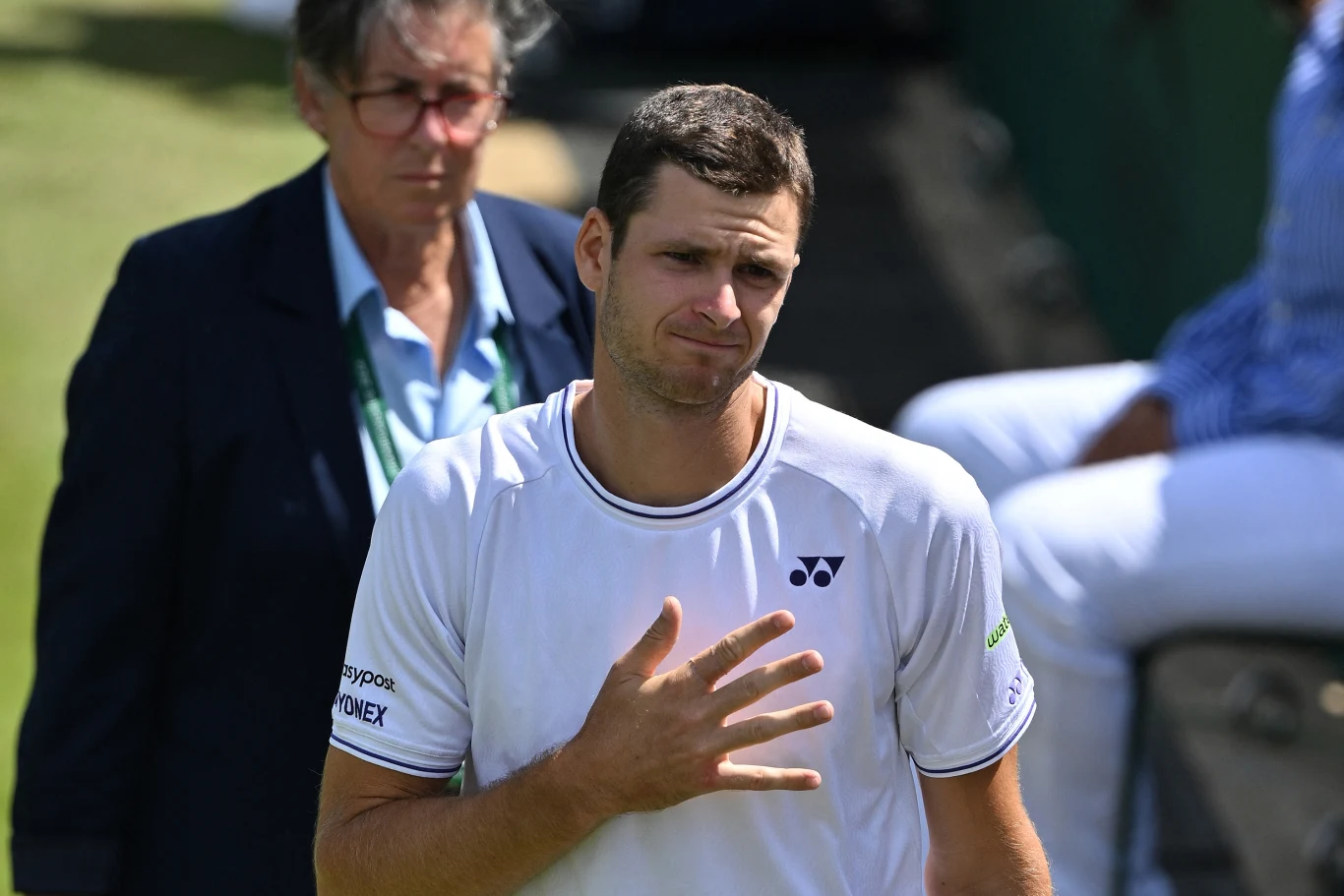 Hubert Hurkacz wycofał się z turnieju ATP Masters 1000 w Cincinnati Mężczyzna w sportowym stroju tenisowym z ręką przy piersi, wyrażający emocje, w tle osoba w garniturze oraz rozmyta sylwetka siedzącej osoby.