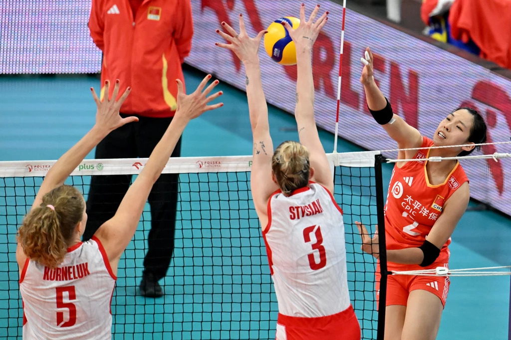 Dzisiejszy mecz Polska - Chiny będzie już trzecim spotkaniem obu drużyn w tym sezonie Dynamiczny moment podczas meczu siatkówki, w którym zawodniczka drużyny w czerwonych strojach atakuje piłkę nad siatką, a dwie siatkarki drużyny w białych koszulkach próbują ją zablokować.
