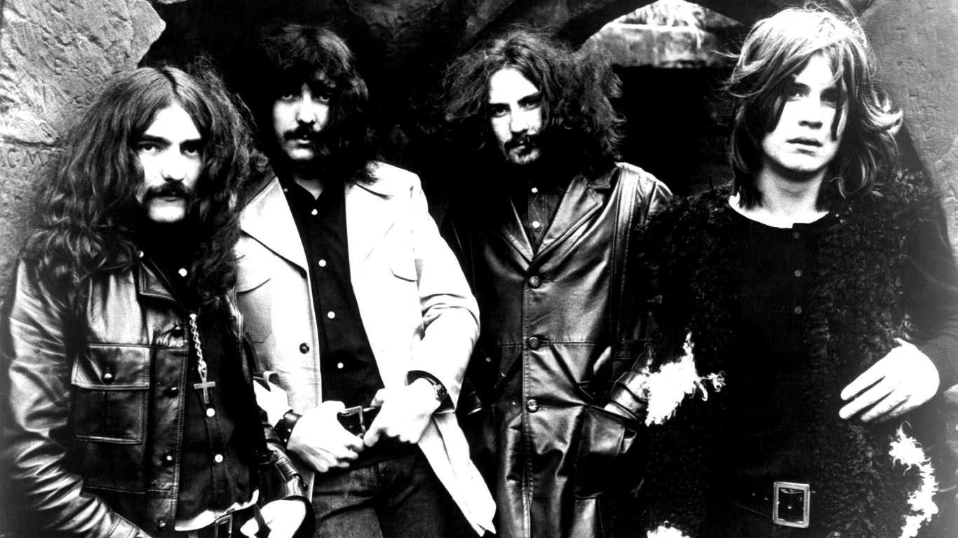 Black Sabbath 1970 Czterech mężczyzn z długimi włosami pozuje razem w ciemnych, skórzanych ubraniach na tle kamiennego łuku, atmosfera utrzymana w klimacie lat 70.