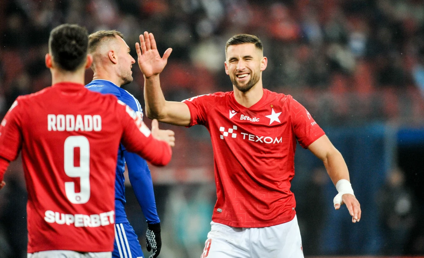 Łukasz Zwoliński i Angel Rodado stanowili skuteczny duet napastników Wisły Kraków Piłkarze drużyny piłkarskiej w czerwonych koszulkach świętują udaną akcję na boisku, jeden z zawodników unosi rękę do przybicia piątki, na drugim planie także bramkarz w niebieskim stroju.