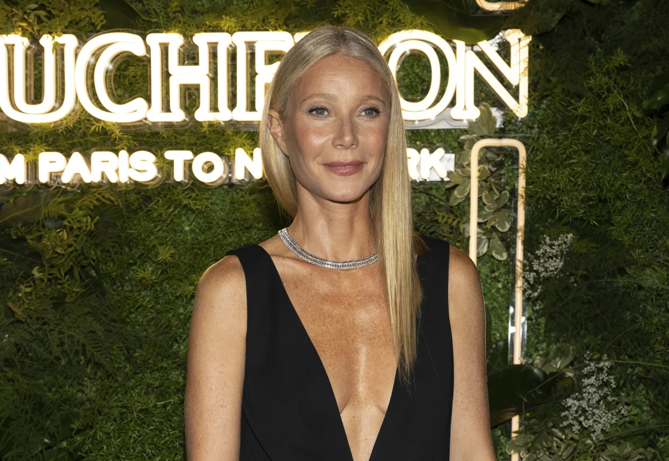Gwyneth Paltrow znana jest z zamiłowania do zdrowej diety Kobieta z długimi blond włosami ubrana w elegancką czarną suknię z głębokim dekoltem pozuje na tle zielonej ściany z podświetlonym napisem.