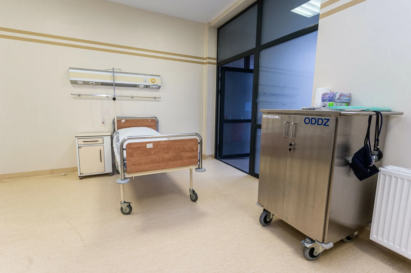 Mieli kontakt z pacjentką z podejrzeniem cholery. Zakończyli kwarantannę (zdj. ilustracyjne) Szpitalna sala z pojedynczym łóżkiem ustawionym obok szafki, metalowa szafa na kółkach z napisem ODDZ, jasne ściany oraz duże przeszklone drzwi prowadzące na korytarz.