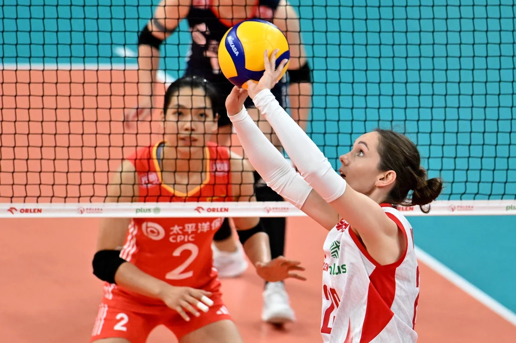 Liga Narodów siatkarek. Katarzyna Wenerska w trakcie sparingu z Chinkami Siatkarka w biało-czerwonym stroju odbija piłkę tuż przy siatce, naprzeciwko której znajduje się zawodniczka drużyny przeciwnej w czerwonym stroju, skupiająca uwagę na piłce, rozgrywka odbywa się podczas meczu siatkówki.