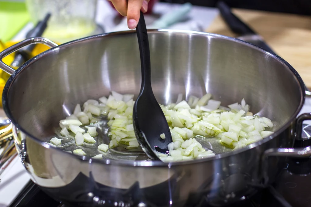 Przygotowanie lecza zacznij od podsmażenia cebuli Pokrojona cebula smażona na oliwie w dużej stalowej patelni, mieszana czarną plastikową łyżką.