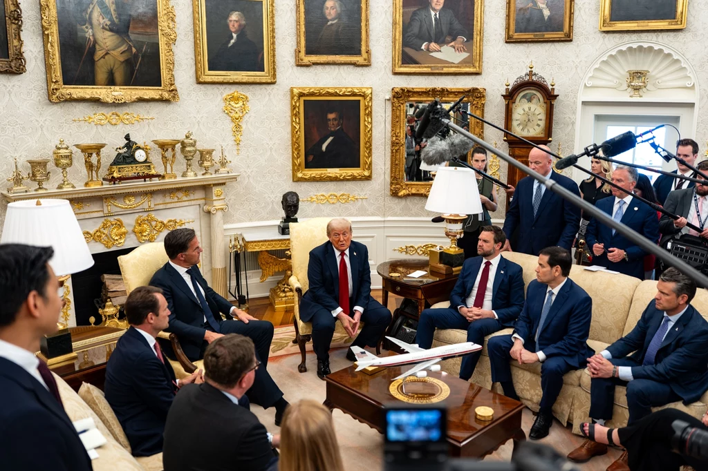 W lipcu Trump spotkał się w Białym Domu z Markiem Ruttem, sekretarzem generalnym NATO Oficjalne spotkanie polityczne w eleganckim gabinecie, gdzie centralną postacią jest mężczyzna w czerwonym krawacie otoczony przez grupę innych mężczyzn w garniturach, siedzących wokół stołu z modelem samolotu, otoczenie wypełnione portretami historycz...