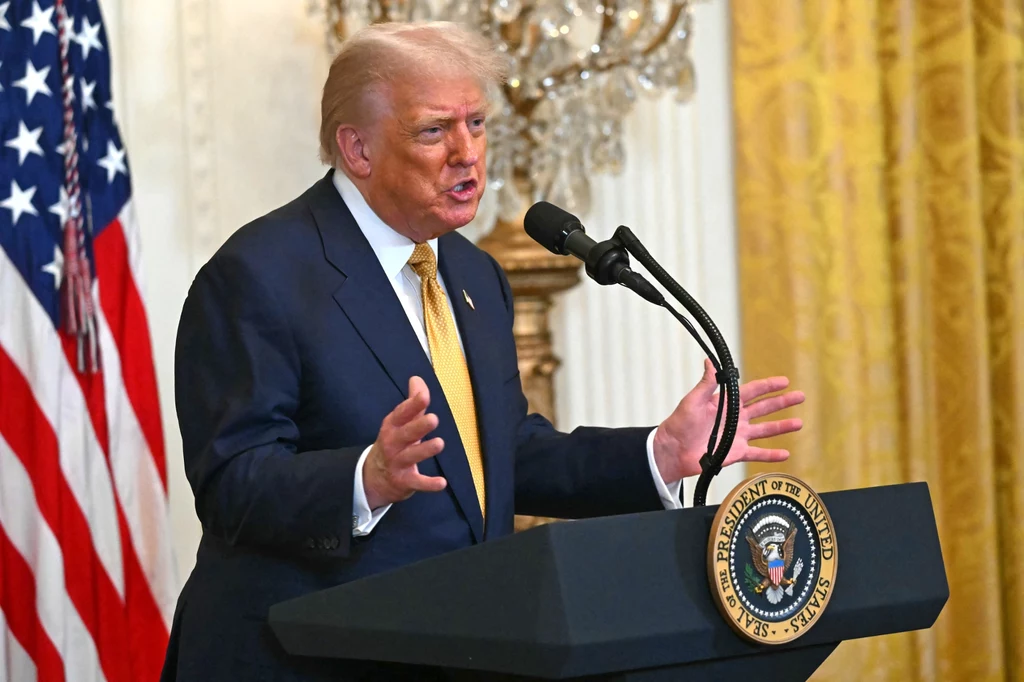 Zdaniem komentatorów Donald Trump jest mocno zirytowany postawą prezydenta Rosji Mężczyzna w garniturze i żółtym krawacie przemawia przy mównicy z godłem prezydenta Stanów Zjednoczonych, w tle amerykańska flaga, złote zasłony i kryształowy żyrandol.
