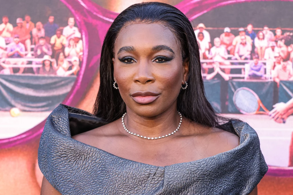 Venus Williams Kobieta o długich, ciemnych włosach ubrana w elegancką suknię z szerokim kołnierzem, ma na szyi subtelny naszyjnik z pereł; tło stanowi kolorowy plakat z motywem okularów przeciwsłonecznych i trybuną tenisową.
