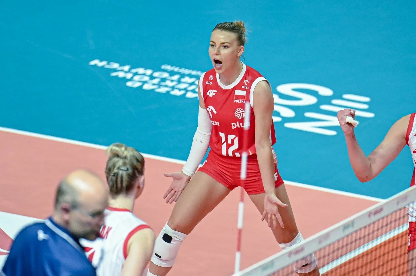 Aleksandra Szczygłowska jest jedną z liderek polskiej kadry Siatkarka w czerwonym stroju z numerem 17 wyraża emocje podczas meczu, wokół niej widoczne są inne zawodniczki w sportowych strojach na tle boiska do siatkówki.