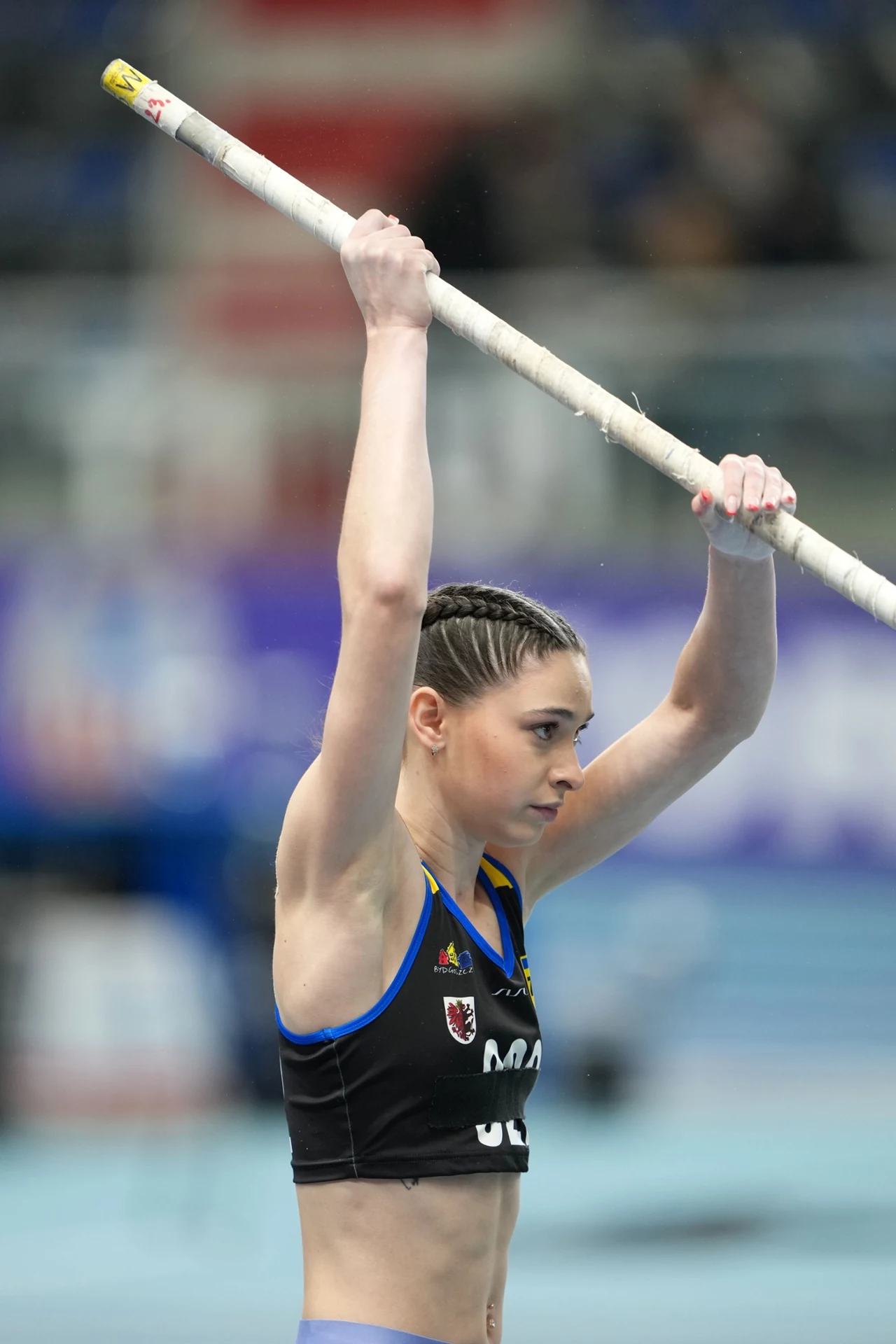 Walentyna Jakowienko Lekkoatletka w stroju sportowym przygotowuje się do skoku o tyczce, trzymając tyczkę obiema rękami nad głową na hali sportowej.