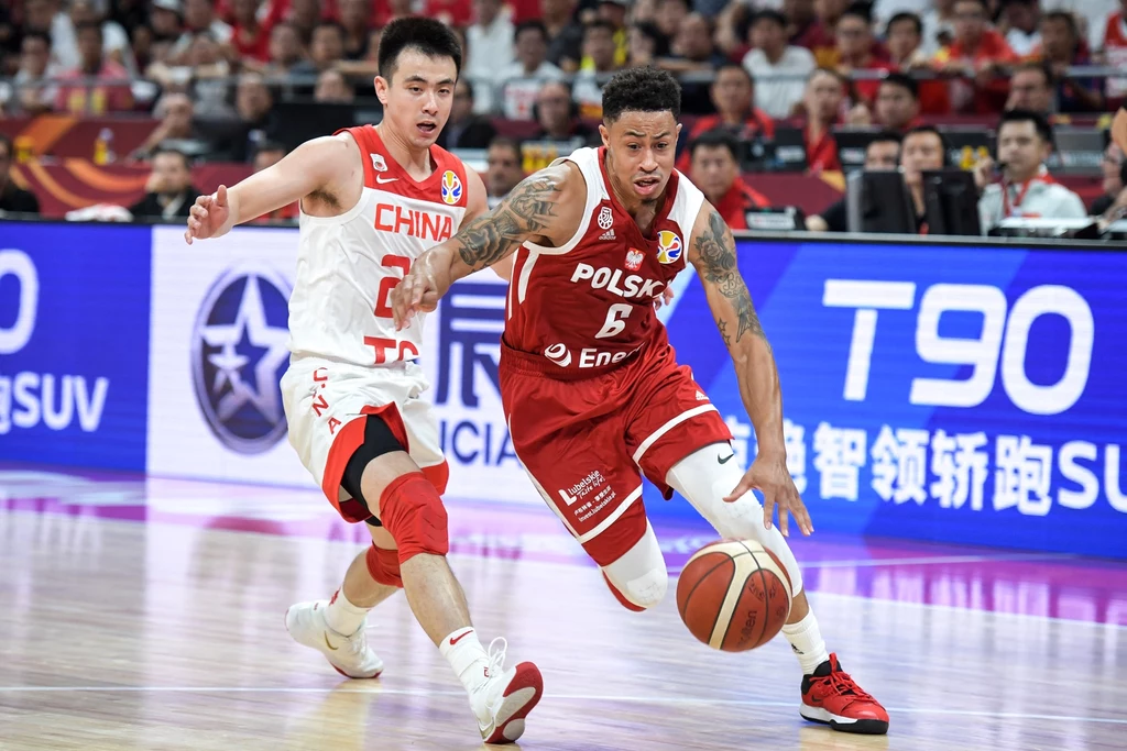 A.J. Slaughter w akcji Dwóch koszykarzy w trakcie intensywnej akcji podczas meczu, zawodnik w czerwonym stroju z Polski prowadzi piłkę, a gracz z Chin próbuje go zatrzymać, dynamiczne otoczenie sportowe z widownią w tle.