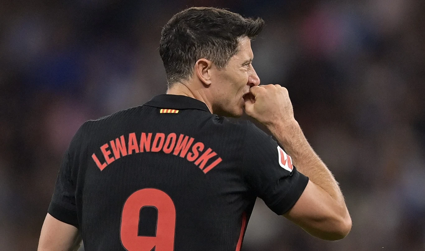 Piłkarz w czarnej koszulce z numerem 9 i nazwiskiem Lewandowski wykonuje charakterystyczny gest pocałowania dłoni, stojąc na boisku podczas meczu.