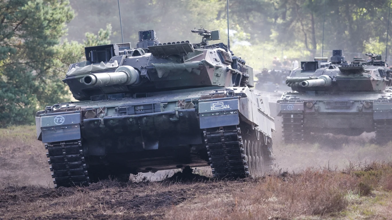 Dodatkowe fundusze na naprawę ukraińskich czołgów w Polsce Dwa czołgi poruszające się po leśnym, błotnistym terenie, z wyraźnie widocznymi gąsienicami i lufami skierowanymi do przodu, w tle drzewa i unoszący się kurz.