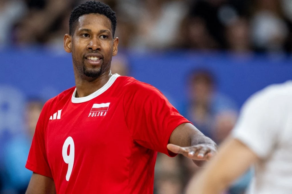 Wilfredo Leon występuje w reprezentacji Polski od 2019 roku Zawodnik siatkarski w czerwonej koszulce z numerem 9 oraz napisem Polska stoi na boisku podczas meczu, skierowany w stronę drużyny przeciwnej, w tle niewyraźne postacie kibiców na trybunach.