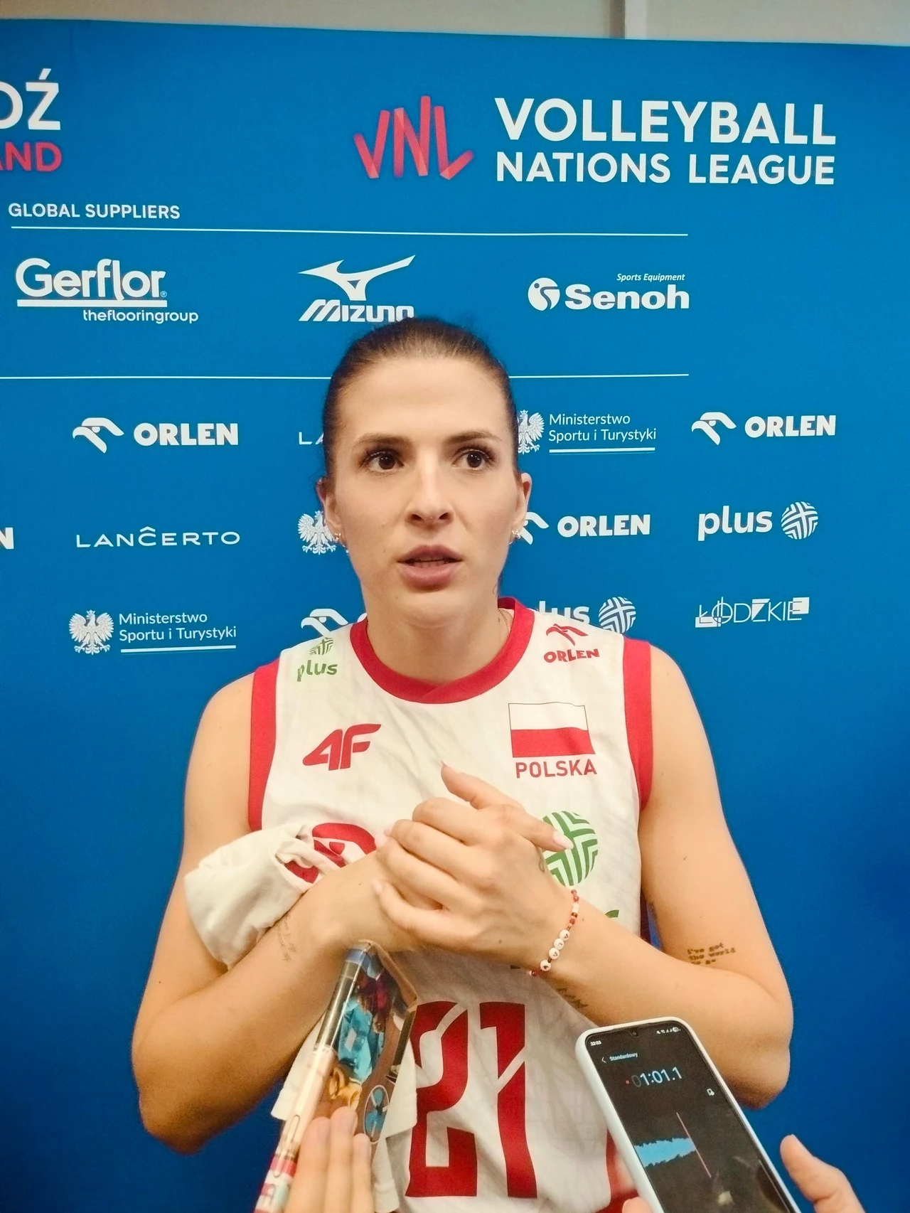Alicja Grabka Polska siatkarka w stroju reprezentacji trzyma ręcznik i odpowiada na pytania dziennikarzy po meczu, w tle niebieska ścianka z logotypami sponsorów oraz informacjami o Volleyball Nations League