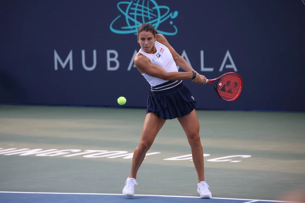 Emma Navarro Tenisistka podczas meczu skupiona na odbieraniu piłki, dynamiczna postawa, profesjonalny strój sportowy, kort tenisowy w tle, charakterystyczny branding turniejowy.