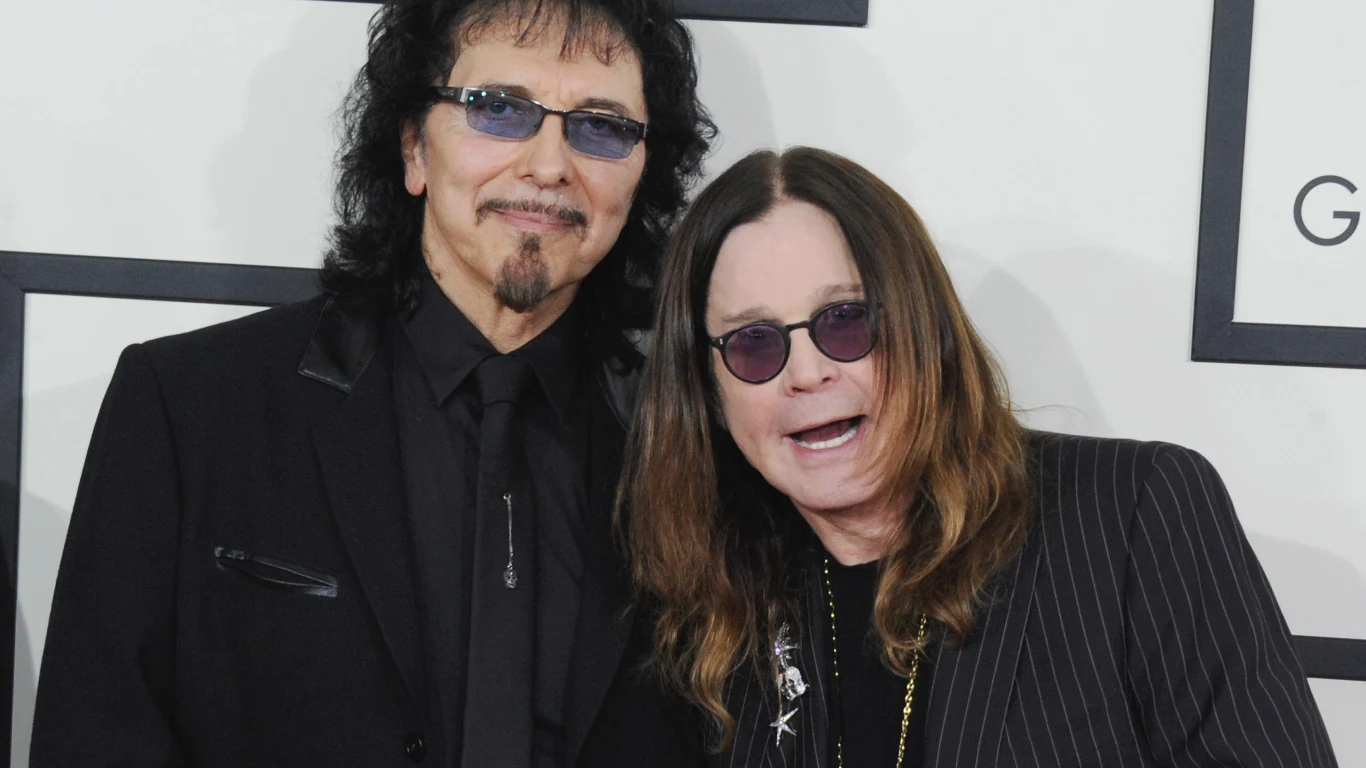 Tony Iommi i Ozzy Osbourne Dwie osoby w ciemnych ubraniach stoją obok siebie, uśmiechają się do kamery, obaj noszą okulary przeciwsłoneczne, w tle widać fragment dekoracji eventu.