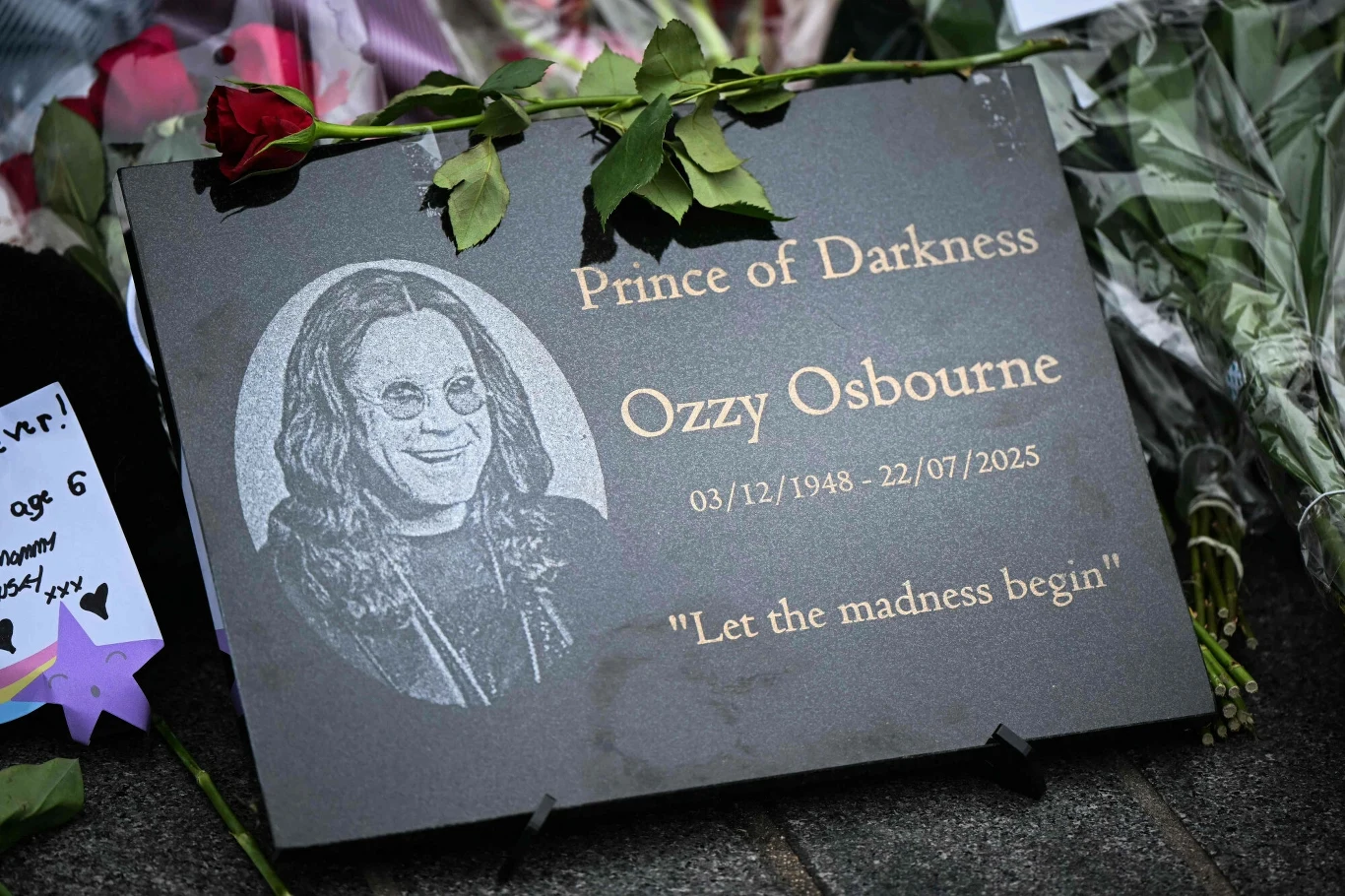 Ozzy Osbourne miał 76 lat Tablica pamiątkowa z wygrawerowanym wizerunkiem Ozzy'ego Osbourne'a, pseudonimem Prince of Darkness oraz datami życia, otoczona kwiatami i pamiątkowymi przedmiotami składanymi przez fanów.