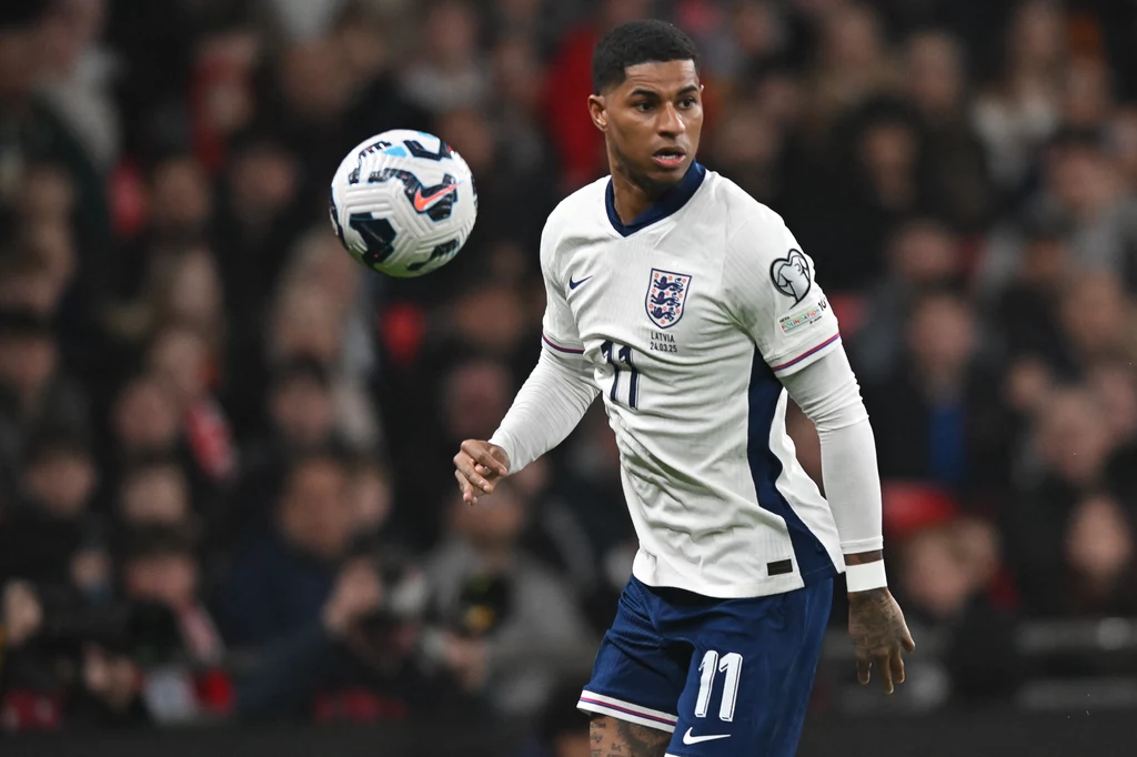 Marcus Rashford Piłkarz w białym stroju reprezentacji Anglii podczas meczu, z numerem 11 na koszulce, skupiony na futbolówce unoszącej się w powietrzu na tle rozmytego stadionu.
